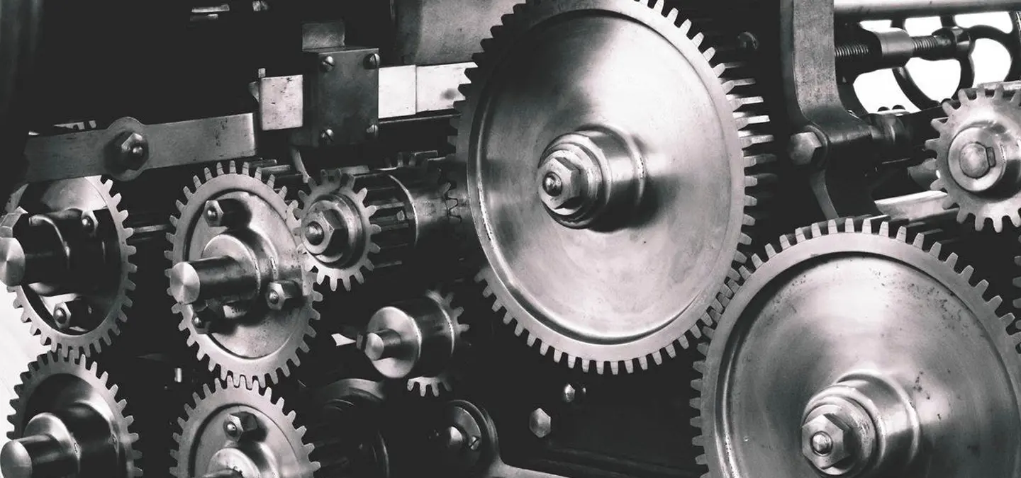 Industrial mechanical gears and cogs in black and white, showing detailed engineering machinery components